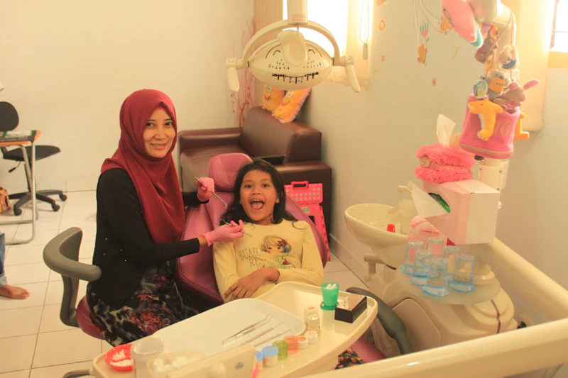 A girl in a dental chair smiling during a check-up, with a dentist beside her