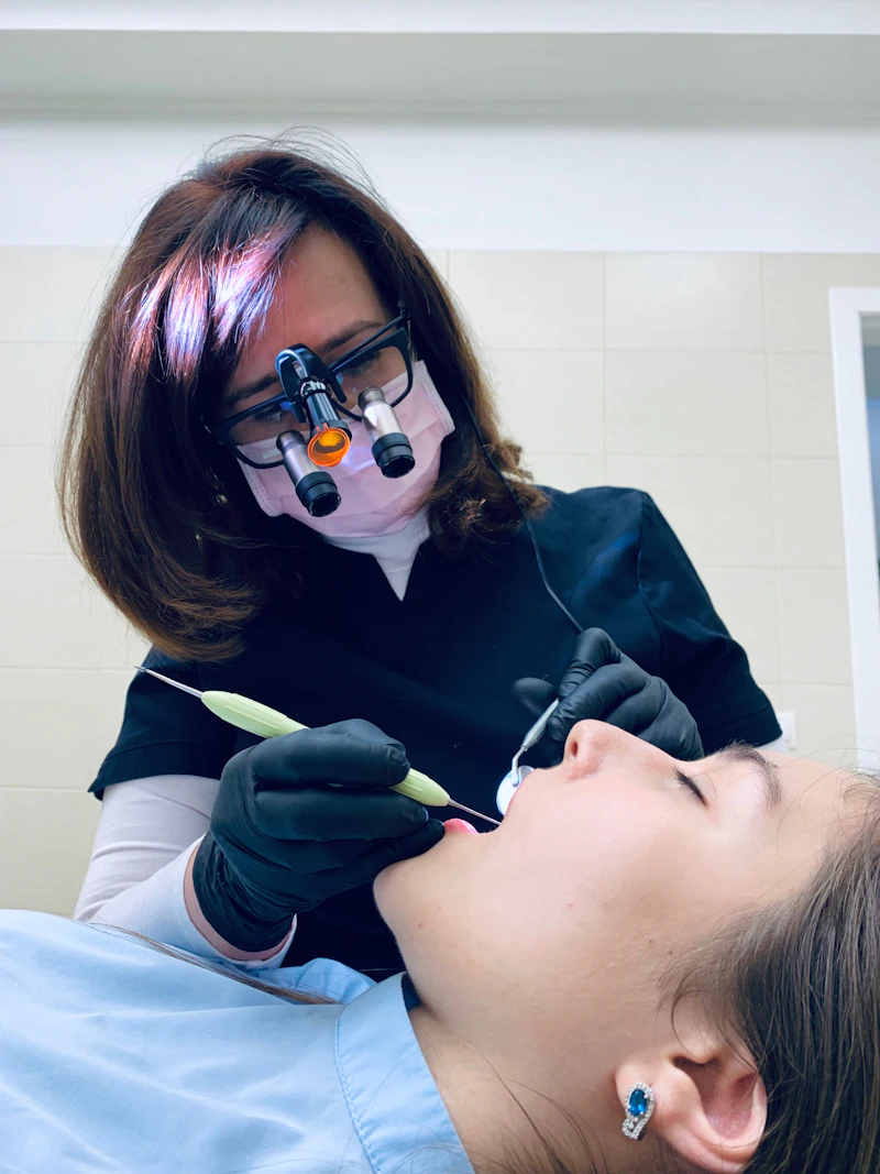 A woman dentist wearing magnifying glasses working on a patient's teeth